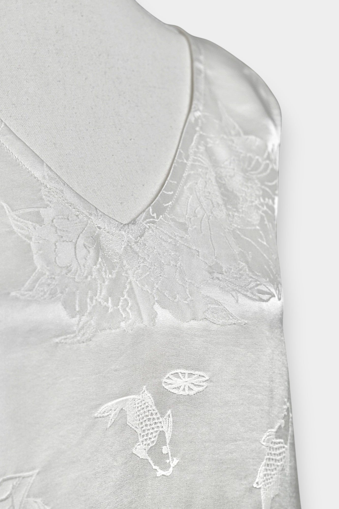 Women's white silk V-neck top with subtle woven koi fish and lotus flower jacquard patterns.