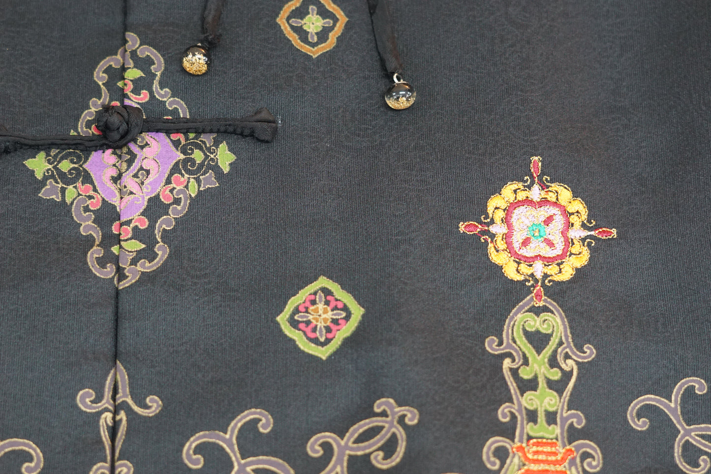 Women's black Song Brocade vest with a mandarin collar, frog buttons, and colorful woven traditional patterns on the hem.