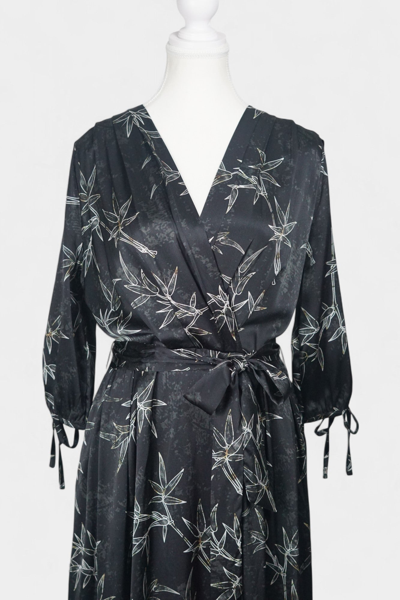Women's black Gambiered Guangdong Gauze wrap dress with white bamboo leaf print and tie-cuff sleeves.