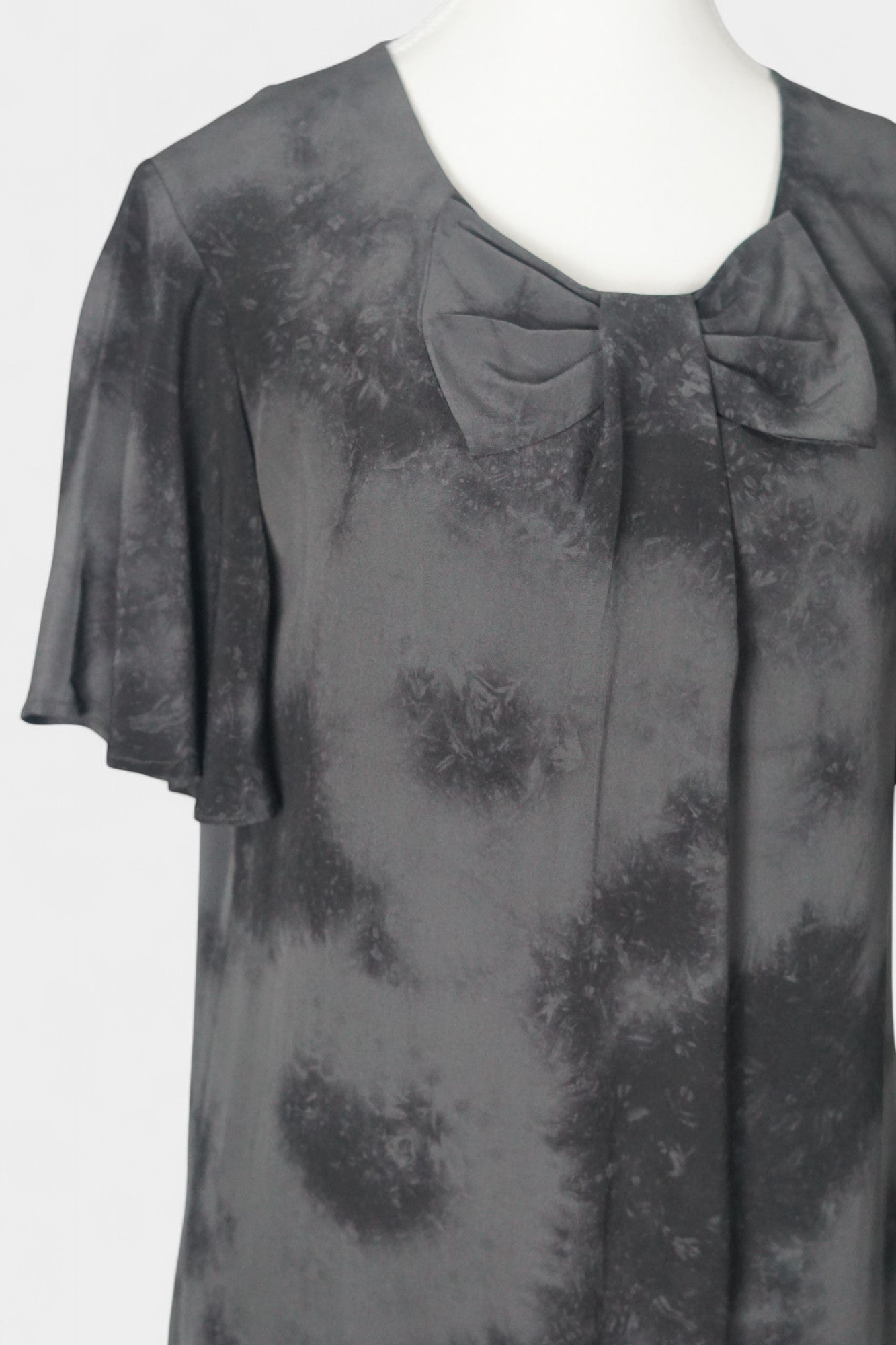 Women's black and grey patterned silk dress with a bow neckline and short flutter sleeves on a mannequin.