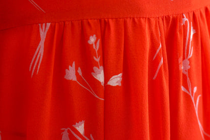 Women's red silk dress with white floral print, featuring a V-neck, wide waistband, and long sheer sleeves