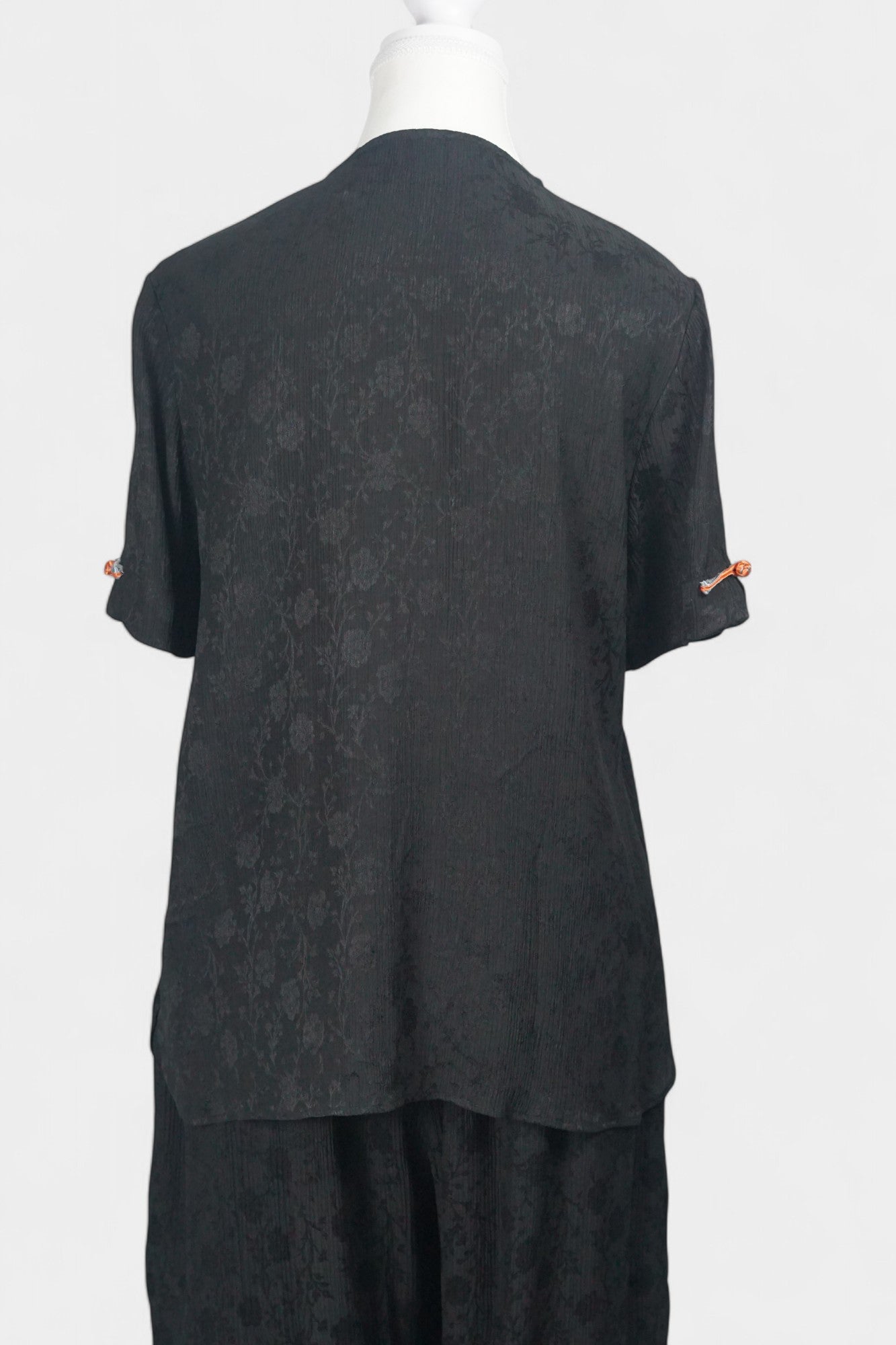 Black textured silk two-piece set featuring a short-sleeve top with contrast frog buttons and matching lantern pants.