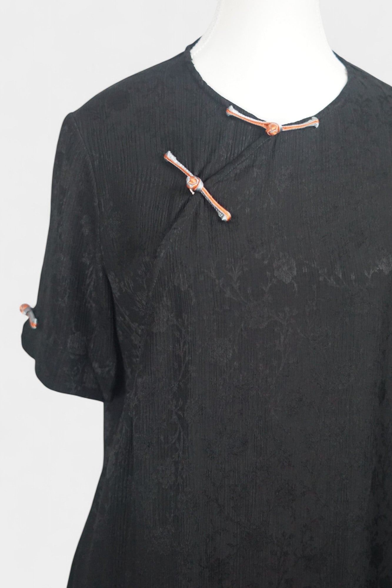 Black textured silk two-piece set featuring a short-sleeve top with contrast frog buttons and matching lantern pants.