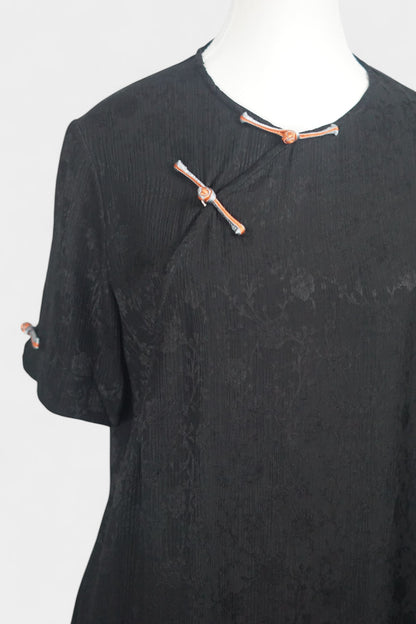 Black textured silk two-piece set featuring a short-sleeve top with contrast frog buttons and matching lantern pants.