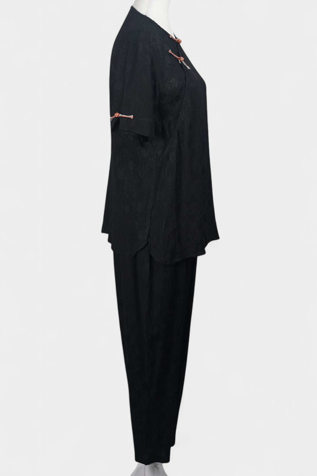 Black textured silk two-piece set featuring a short-sleeve top with contrast frog buttons and matching lantern pants