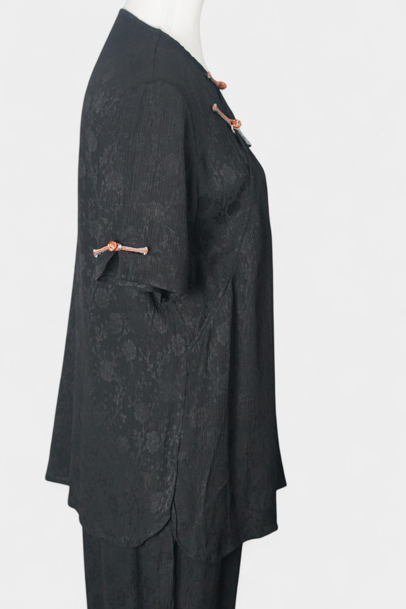 Black textured silk two-piece set featuring a short-sleeve top with contrast frog buttons and matching lantern pants