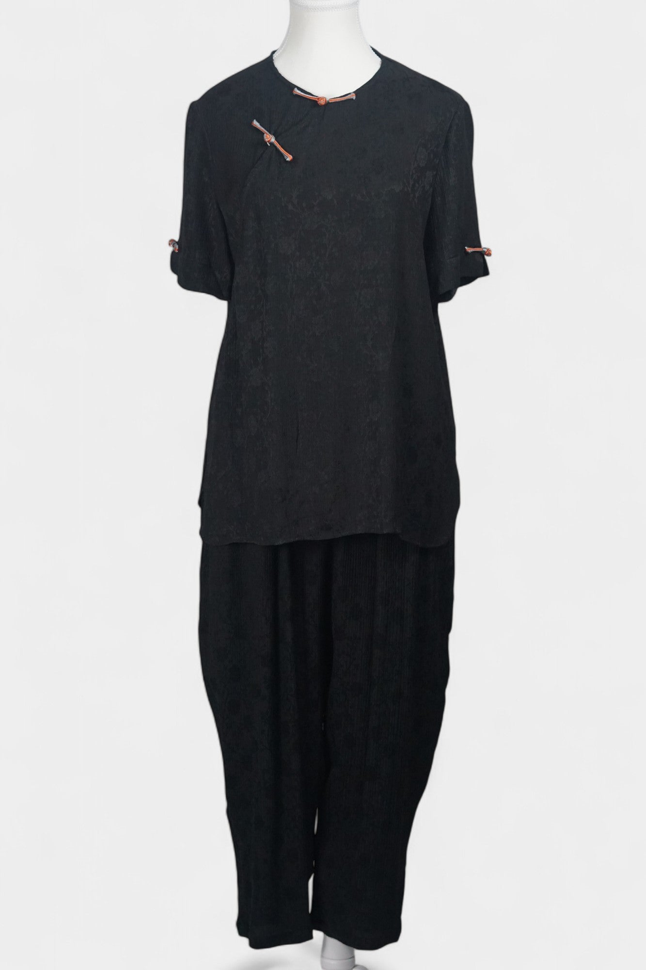 Black textured silk two-piece set featuring a short-sleeve top with contrast frog buttons and matching lantern pants.