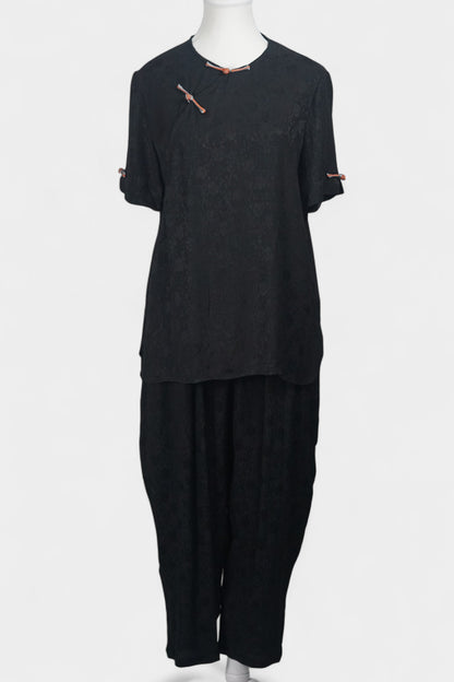 Black textured silk two-piece set featuring a short-sleeve top with contrast frog buttons and matching lantern pants.