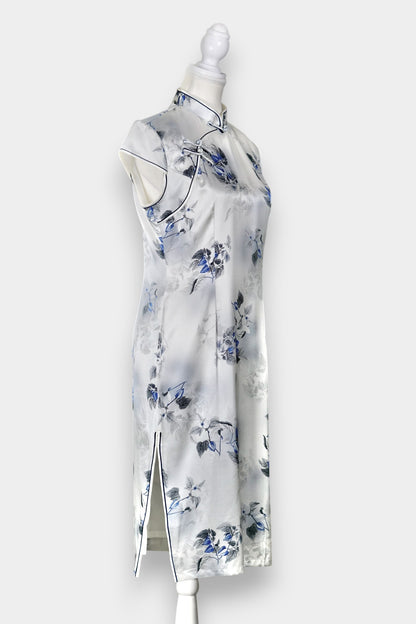 White silk Cheongsam dress featuring a blue and grey ink-wash floral pattern, mandarin collar, and traditional frog buttons on a mannequin.
