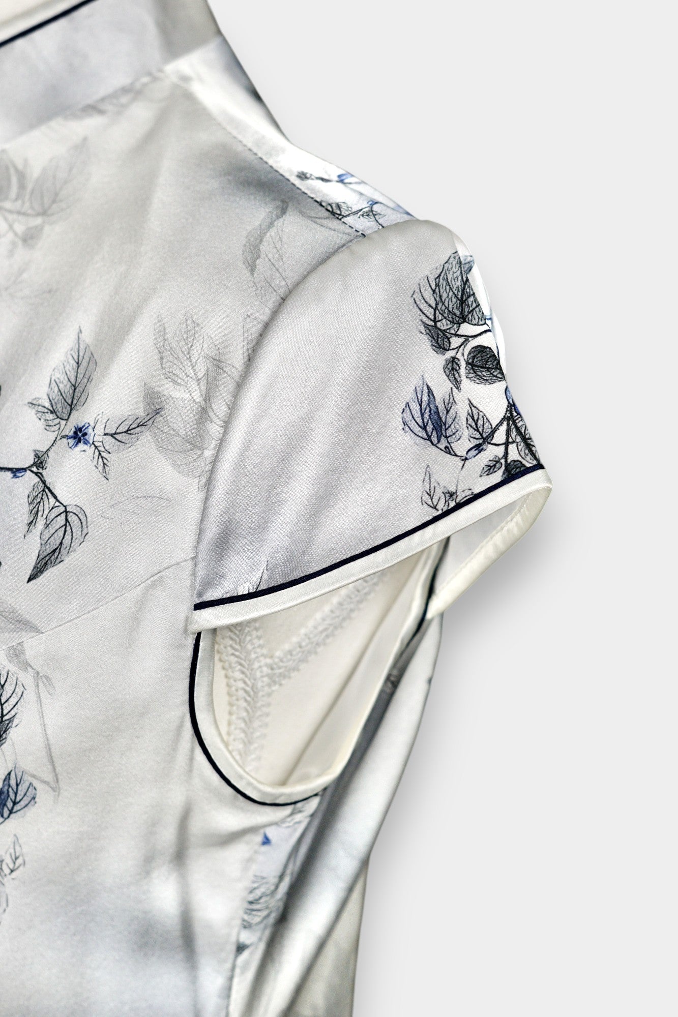 White silk Cheongsam dress featuring a blue and grey ink-wash floral pattern, mandarin collar, and traditional frog buttons on a mannequin.