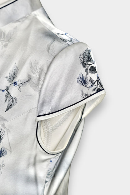 White silk Cheongsam dress featuring a blue and grey ink-wash floral pattern, mandarin collar, and traditional frog buttons on a mannequin.