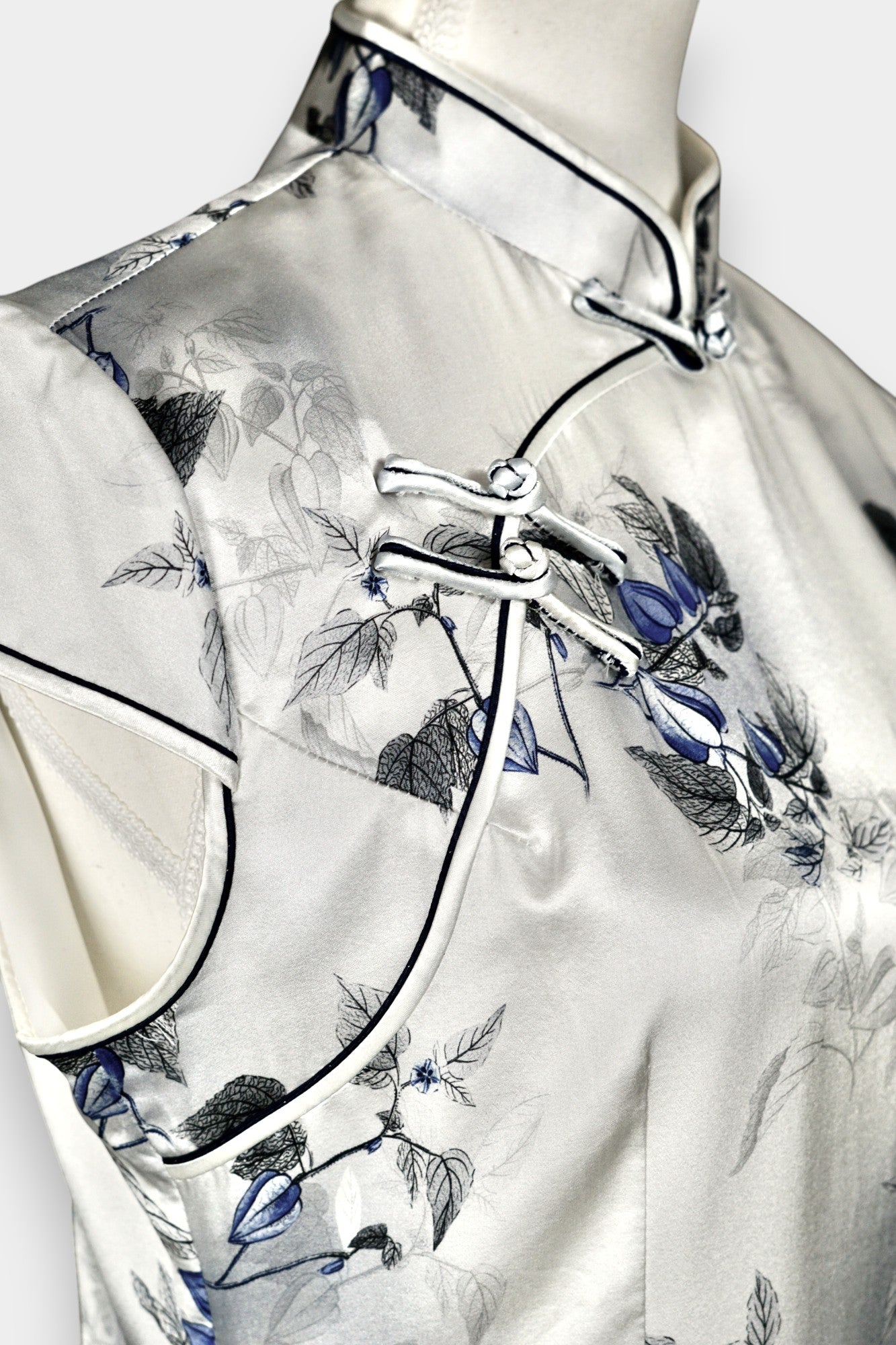 White silk Cheongsam dress featuring a blue and grey ink-wash floral pattern, mandarin collar, and traditional frog buttons on a mannequin.