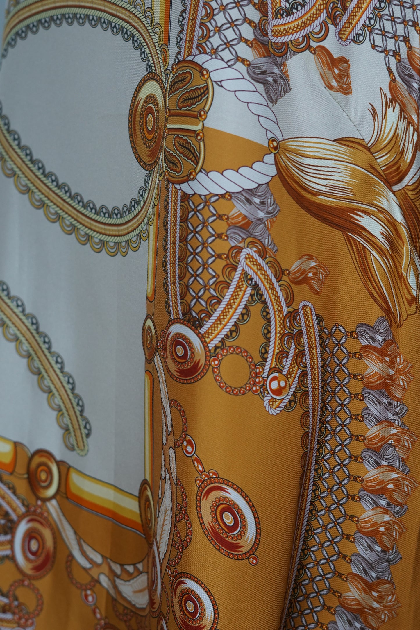 Women's sleeveless beige silk top with gold chain and tassel scarf print and black trim.