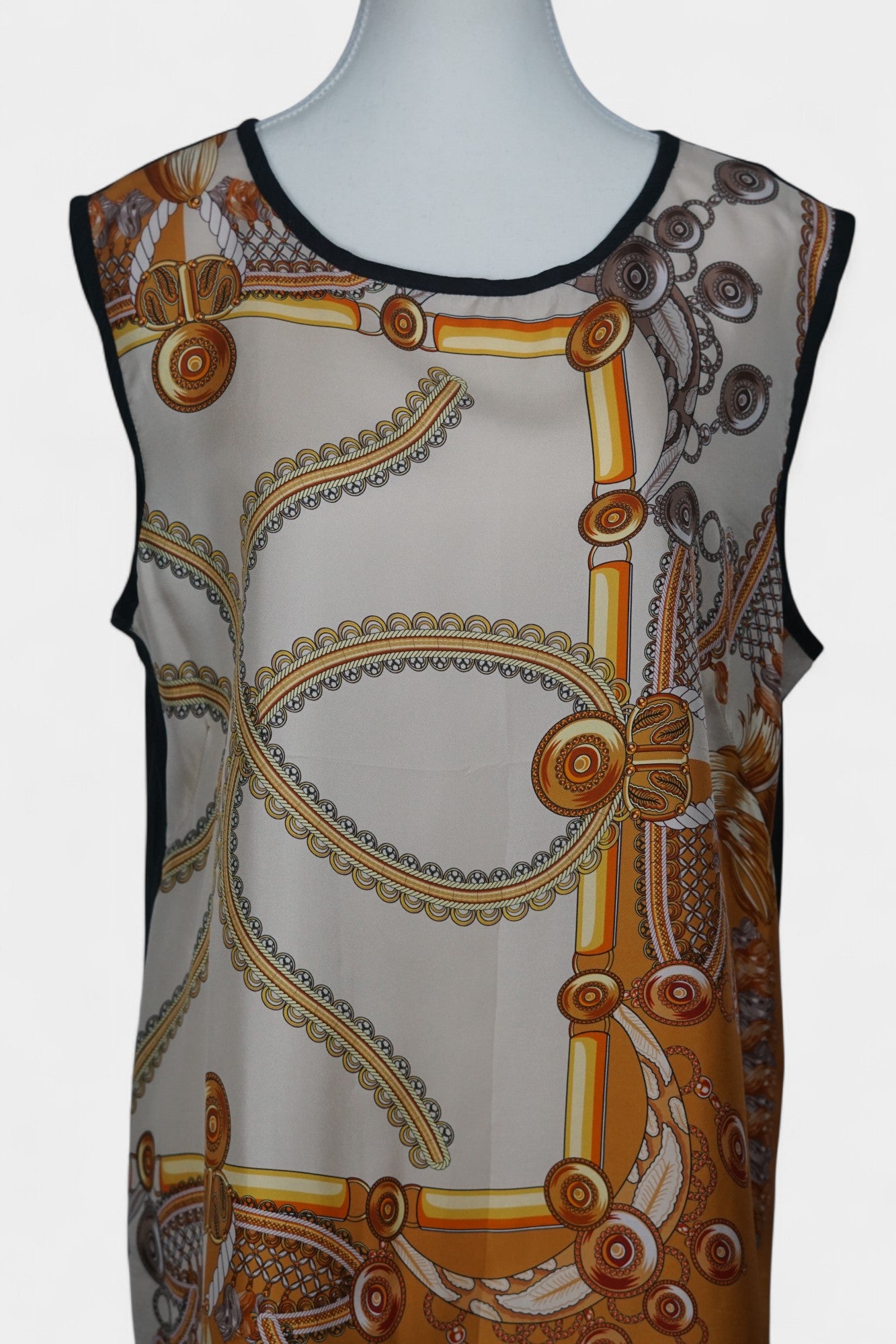 Women's sleeveless beige silk top with gold chain and tassel scarf print and black trim.