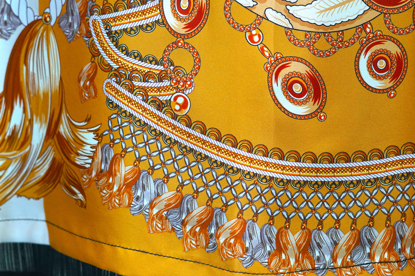 Women's sleeveless beige silk top with gold chain and tassel scarf print and black trim.