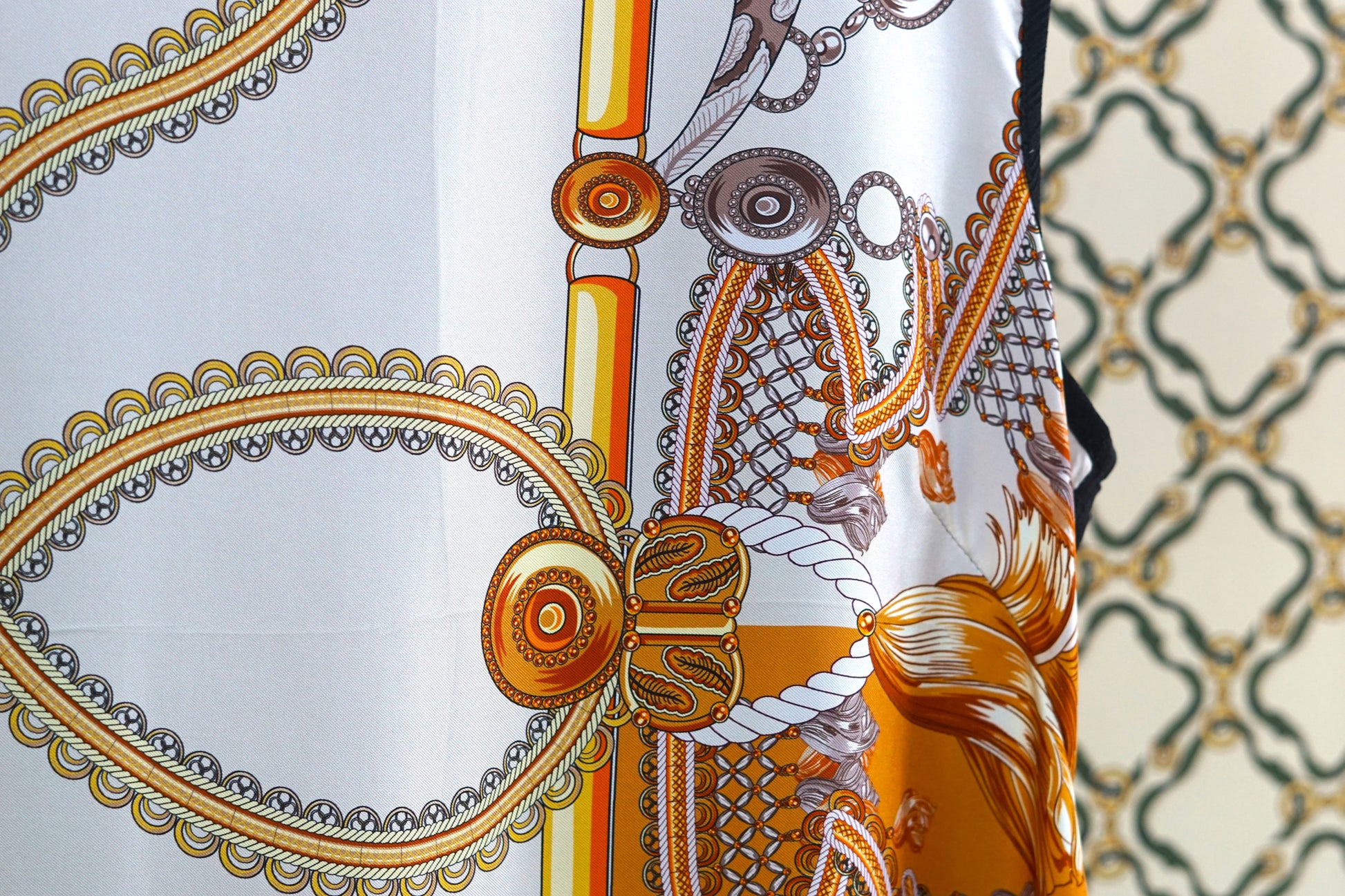 Women's sleeveless beige silk top with gold chain and tassel scarf print and black trim.