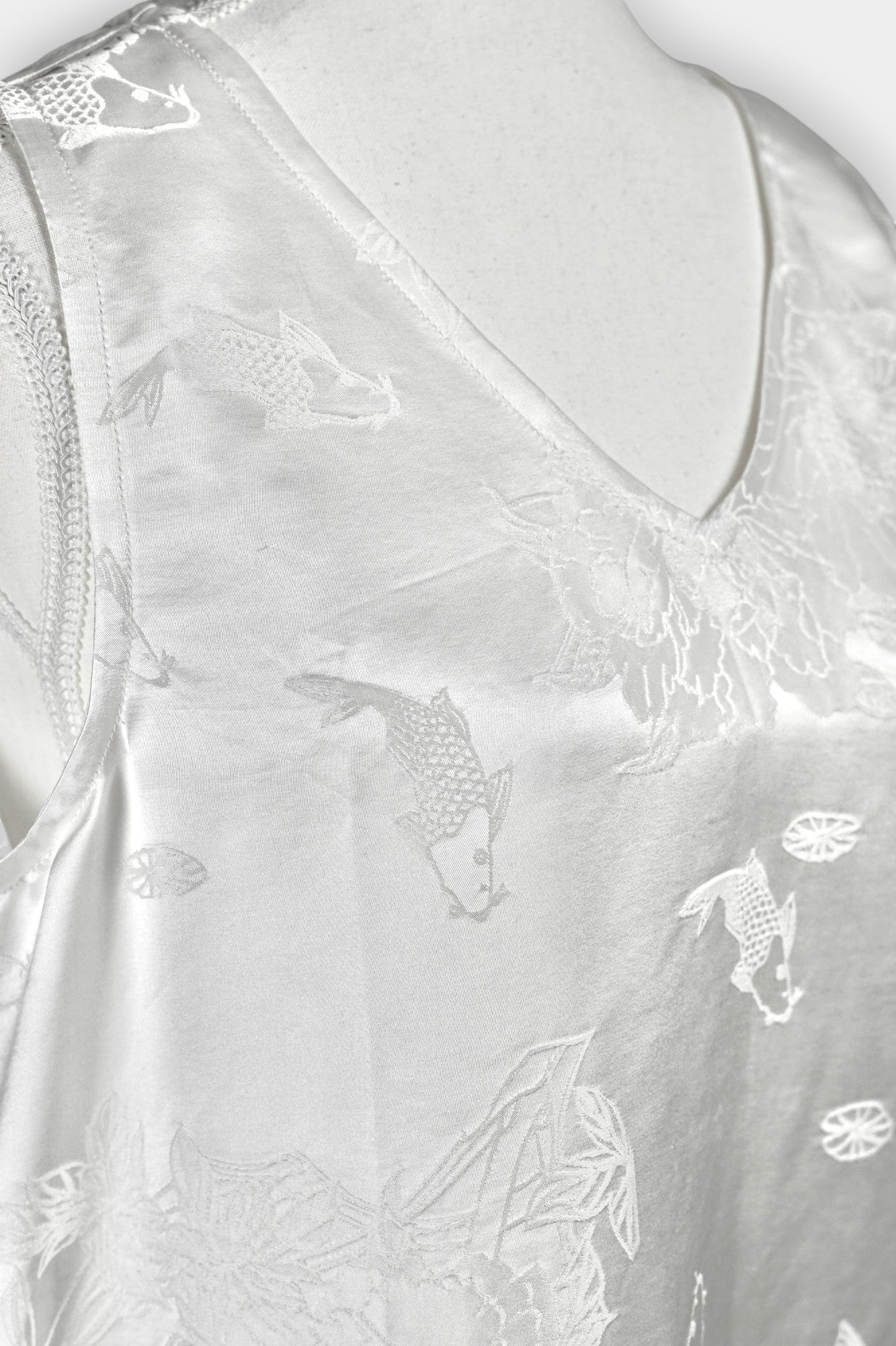 Women's white silk V-neck top with subtle woven koi fish and lotus flower jacquard patterns.