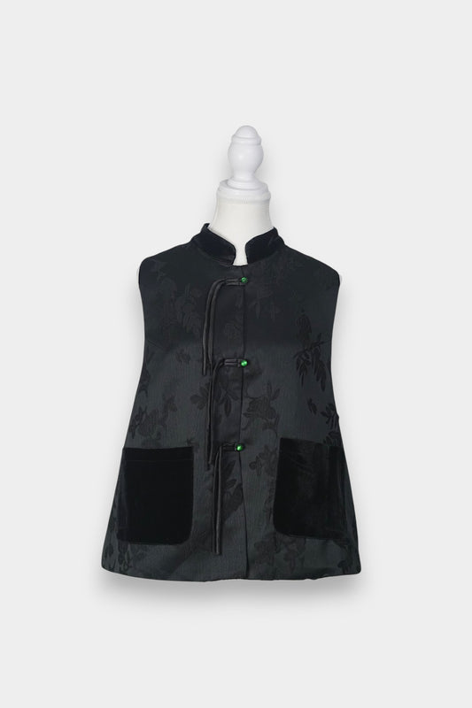 Sleeveless black vest featuring subtle floral jacquard patterns, a velvet Mandarin collar, two velvet patch pockets, and three decorative frog buttons with green beads and long tassels.