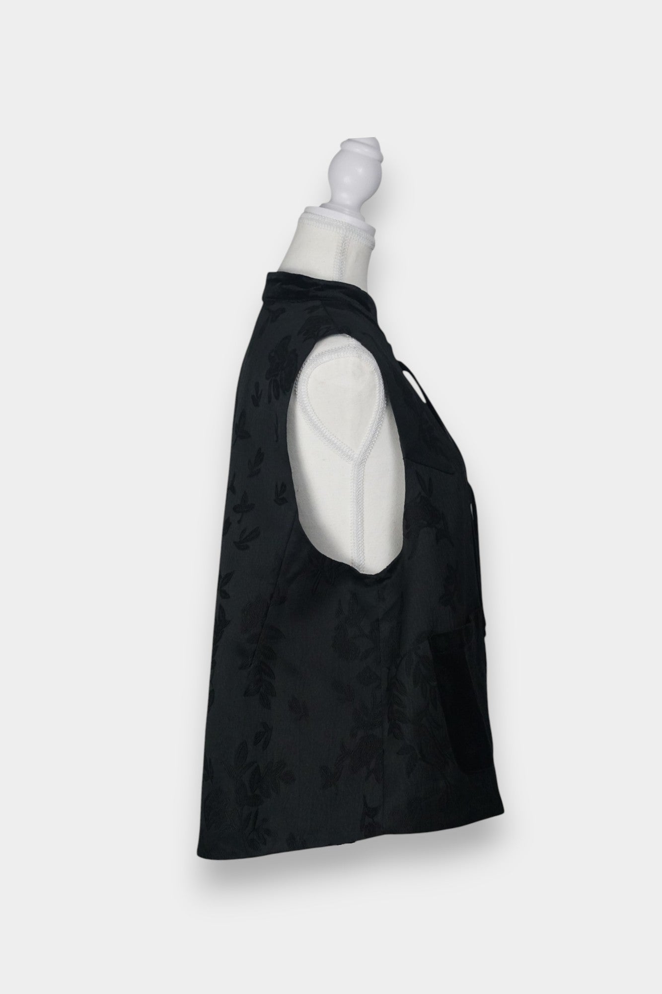 Sleeveless black vest featuring subtle floral jacquard patterns, a velvet Mandarin collar, two velvet patch pockets, and three decorative frog buttons with green beads and long tassels.