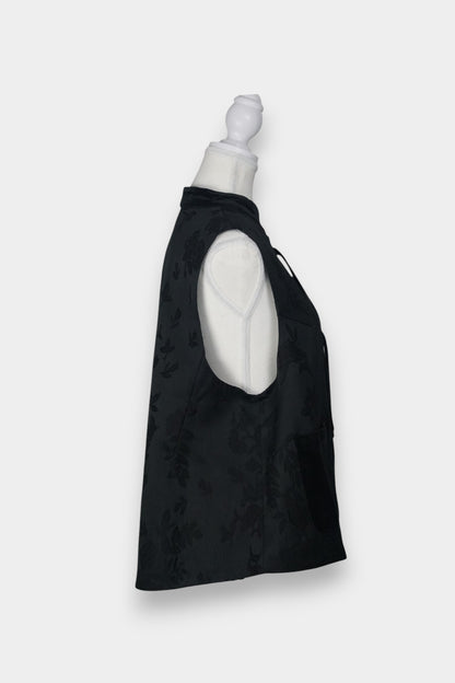 Sleeveless black vest featuring subtle floral jacquard patterns, a velvet Mandarin collar, two velvet patch pockets, and three decorative frog buttons with green beads and long tassels.