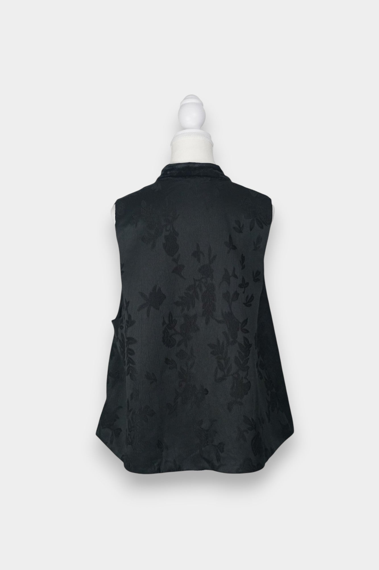 Sleeveless black vest featuring subtle floral jacquard patterns, a velvet Mandarin collar, two velvet patch pockets, and three decorative frog buttons with green beads and long tassels.