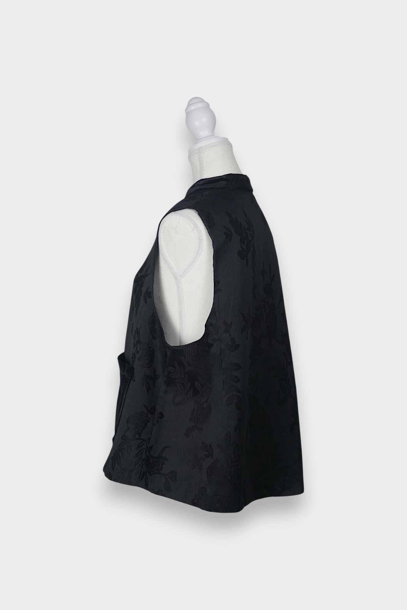 Sleeveless black vest featuring subtle floral jacquard patterns, a velvet Mandarin collar, two velvet patch pockets, and three decorative frog buttons with green beads and long tassels.