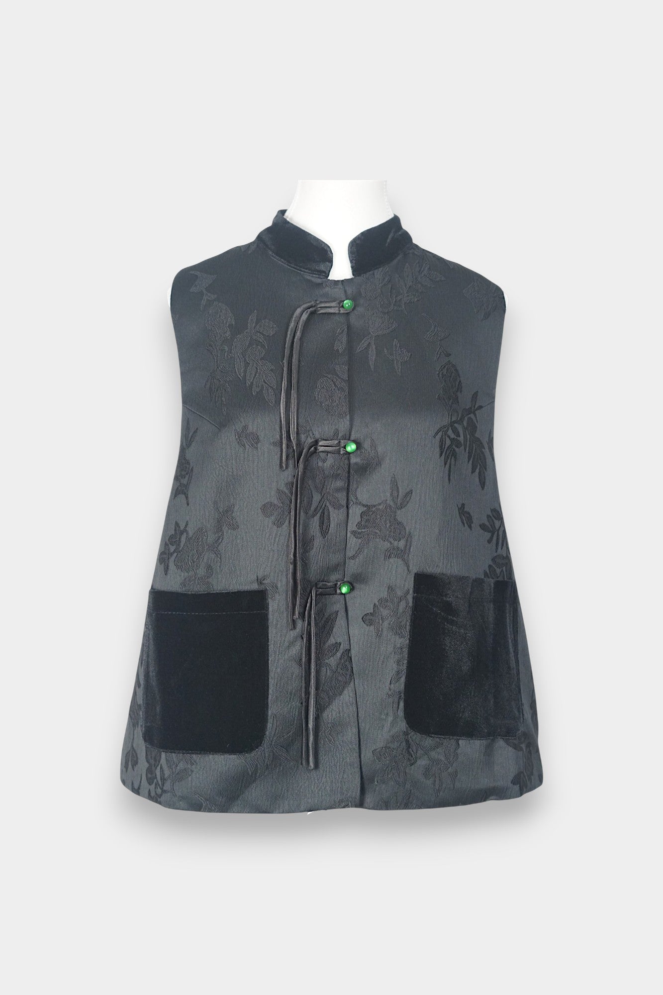Sleeveless black vest featuring subtle floral jacquard patterns, a velvet Mandarin collar, two velvet patch pockets, and three decorative frog buttons with green beads and long tassels.