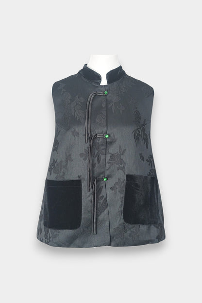 Sleeveless black vest featuring subtle floral jacquard patterns, a velvet Mandarin collar, two velvet patch pockets, and three decorative frog buttons with green beads and long tassels.