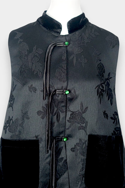 Sleeveless black vest featuring subtle floral jacquard patterns, a velvet Mandarin collar, two velvet patch pockets, and three decorative frog buttons with green beads and long tassels.