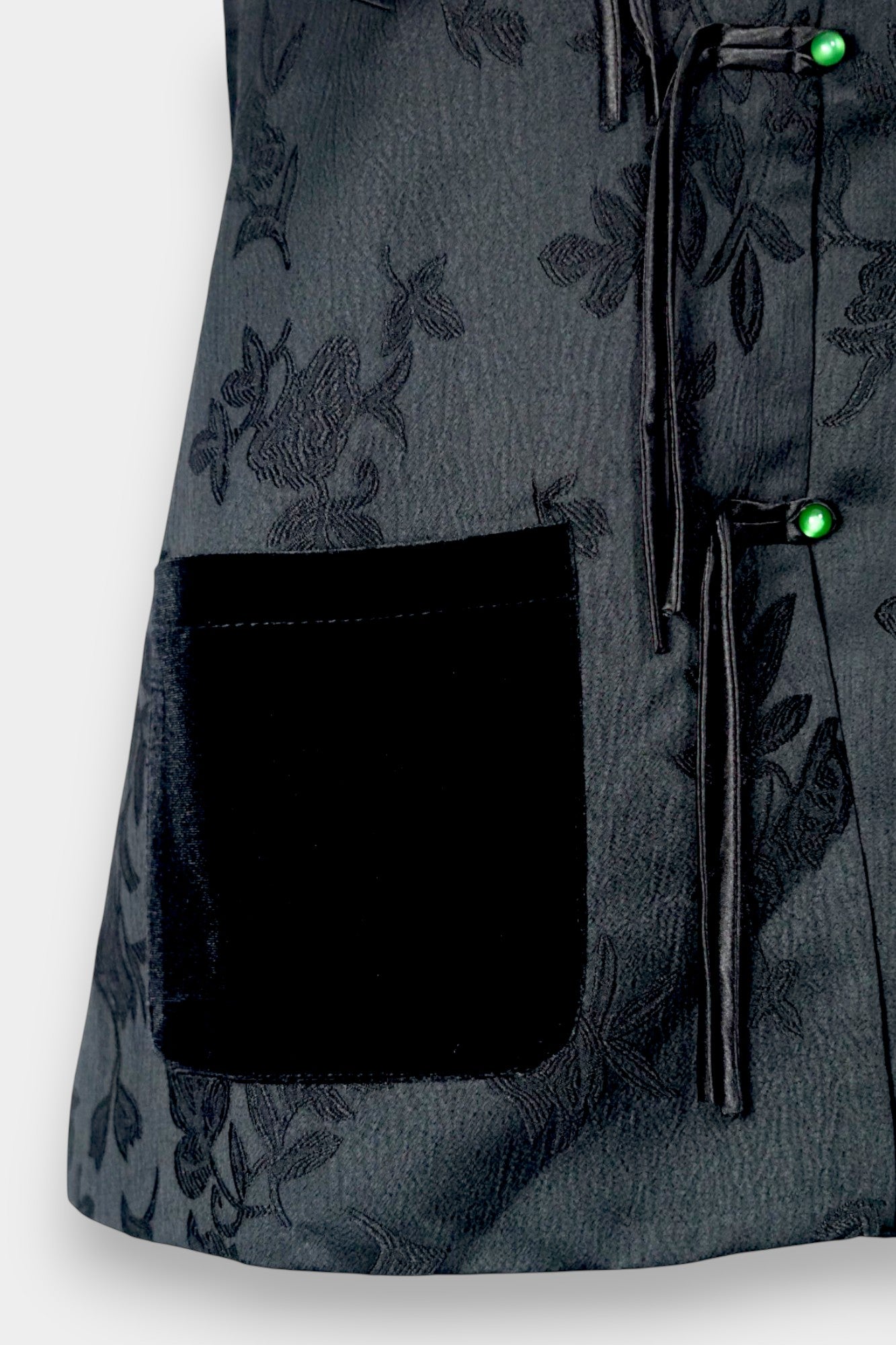 Sleeveless black vest featuring subtle floral jacquard patterns, a velvet Mandarin collar, two velvet patch pockets, and three decorative frog buttons with green beads and long tassels.