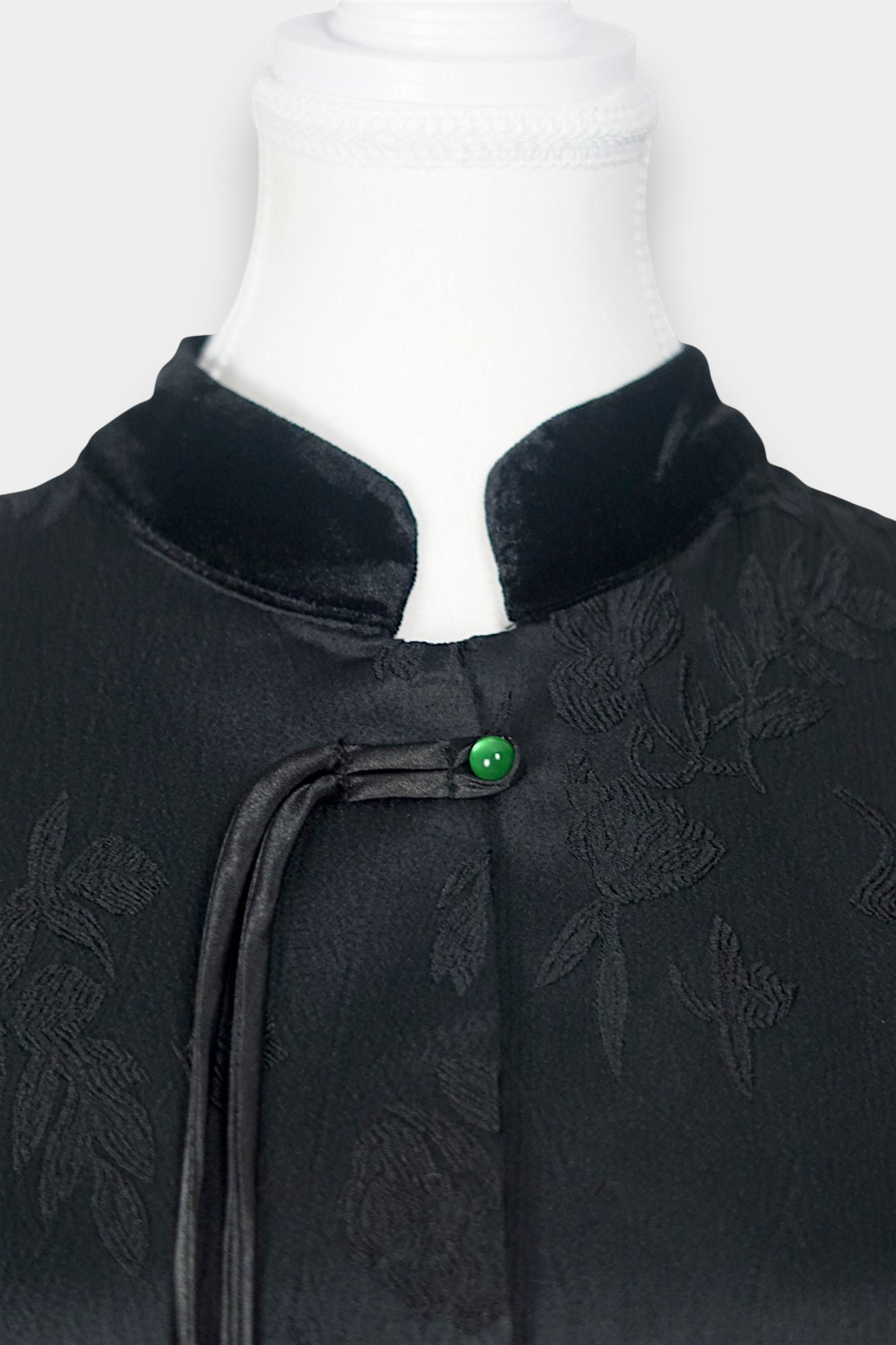 Sleeveless black vest featuring subtle floral jacquard patterns, a velvet Mandarin collar, two velvet patch pockets, and three decorative frog buttons with green beads and long tassels.