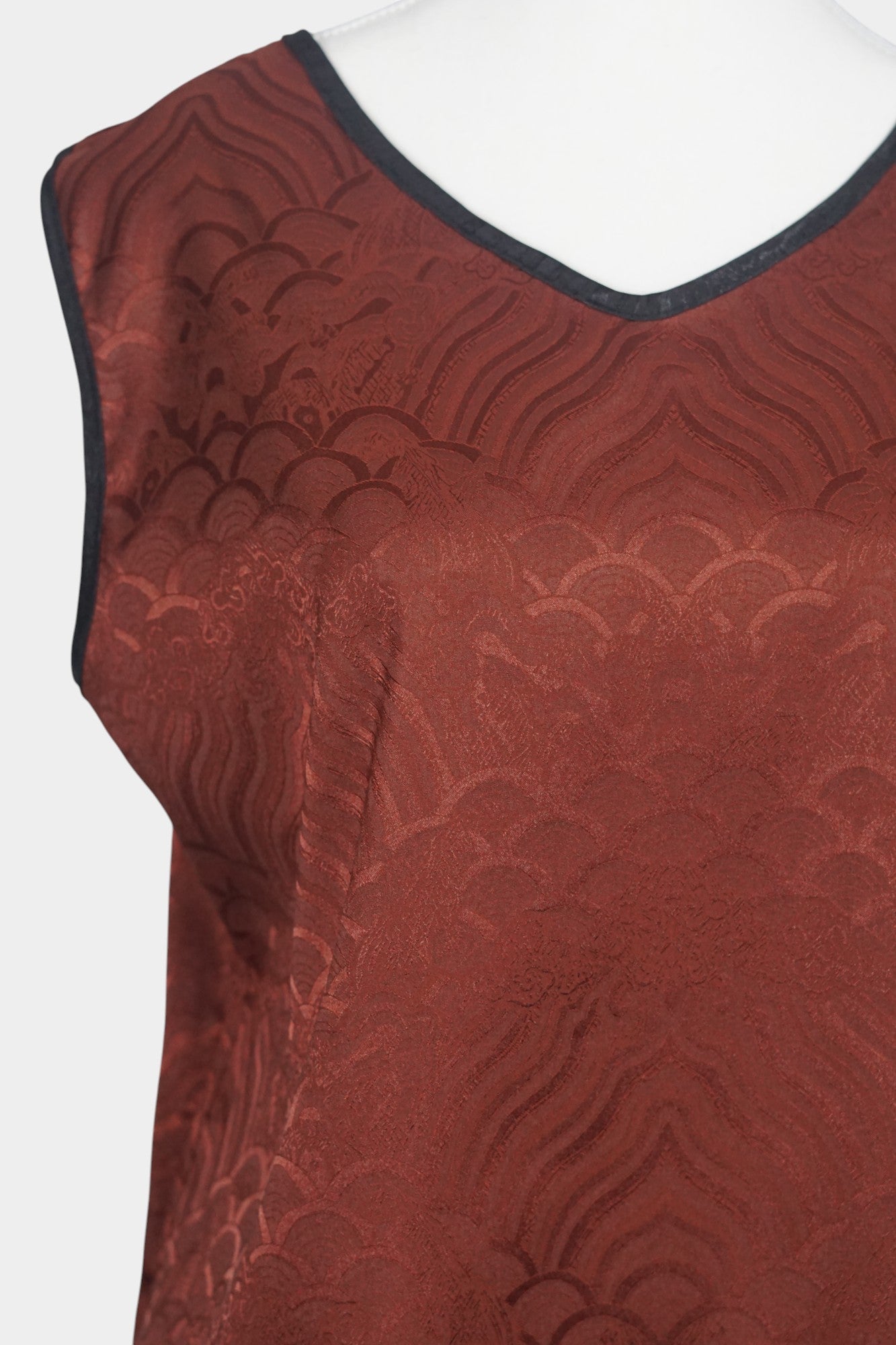 Rust red side of a reversible Gambiered Guangdong Gauze silk vest with black piping trim and traditional cloud pattern