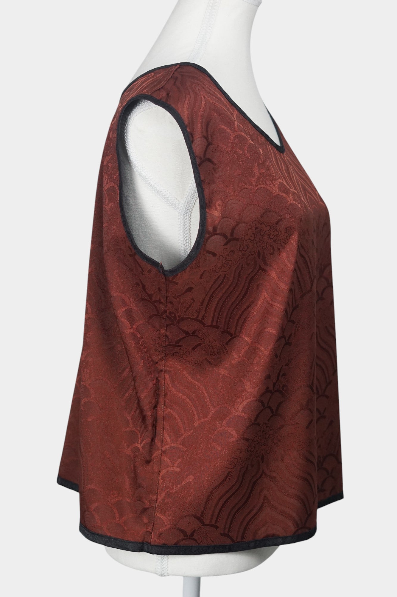 Rust red side of a reversible Gambiered Guangdong Gauze silk vest with black piping trim and traditional cloud pattern.
