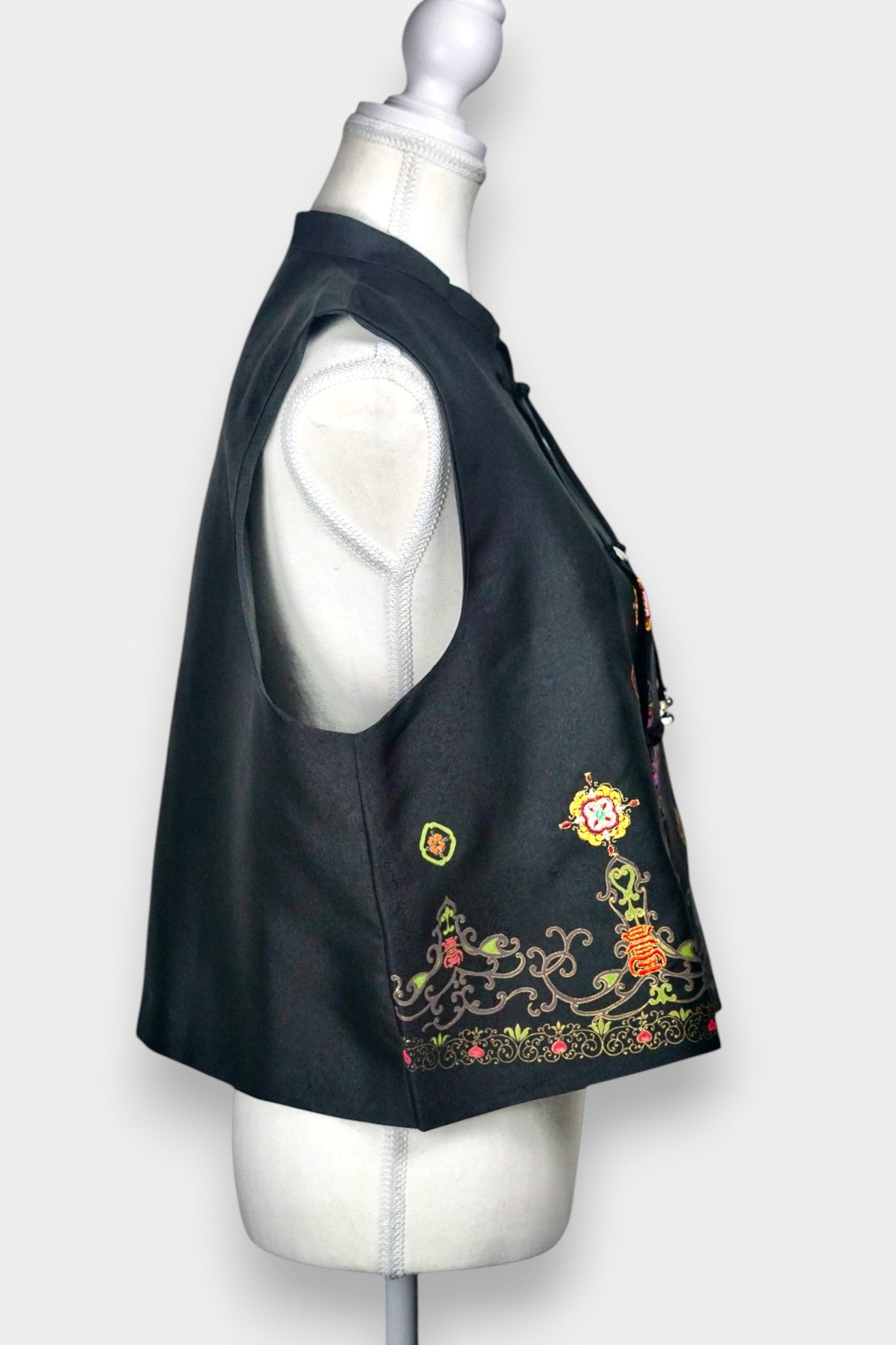 Women's black Song Brocade vest with a mandarin collar, frog buttons, and colorful woven traditional patterns on the hem.