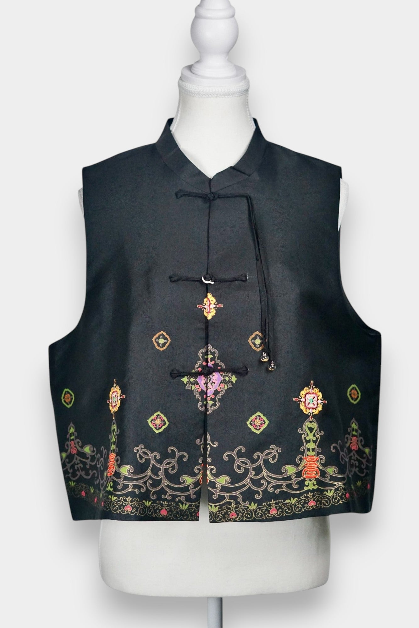 Women's black Song Brocade vest with a mandarin collar, frog buttons, and colorful woven traditional patterns on the hem.