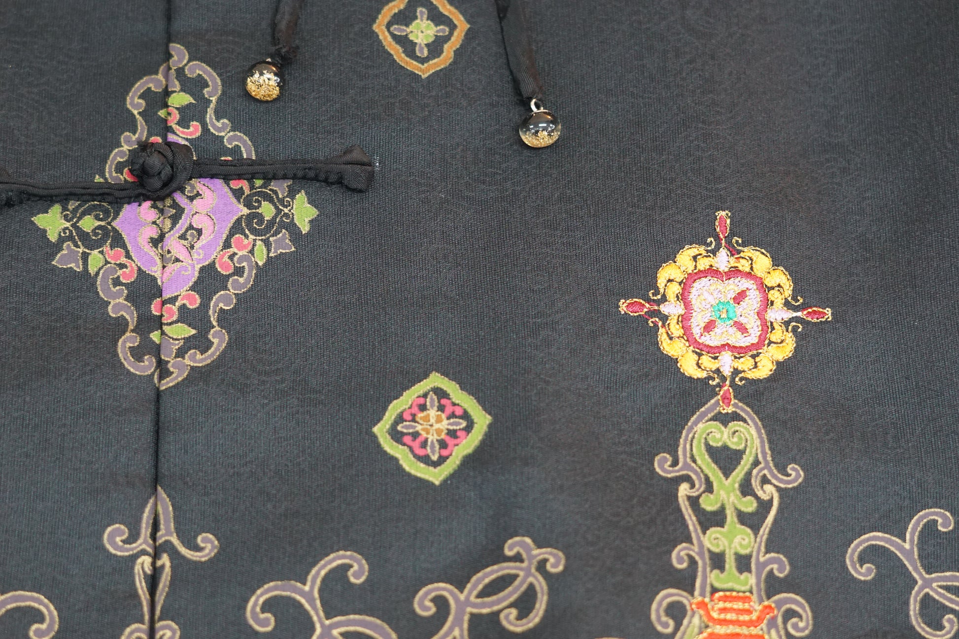 Women's black Song Brocade vest with a mandarin collar, frog buttons, and colorful woven traditional patterns on the hem.