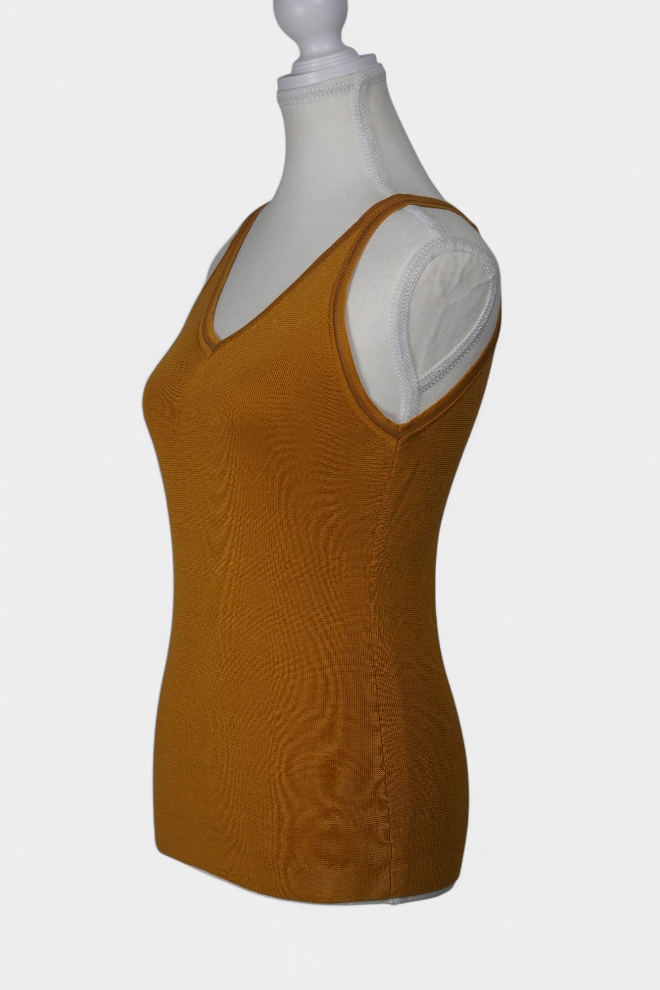 Rear view of a mustard-colored knit tank top on a white mannequin, featuring wide straps and a clean V-shaped neckline at the back.